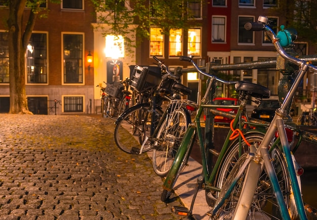 Netherlands. Night Amsterdam. Several bicycles are parked at the canal fence on the cobbled pavement