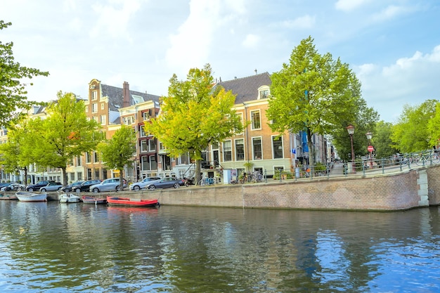 オランダ。アムステルダム運河の春の日。水に係留されたボートと堤防の車