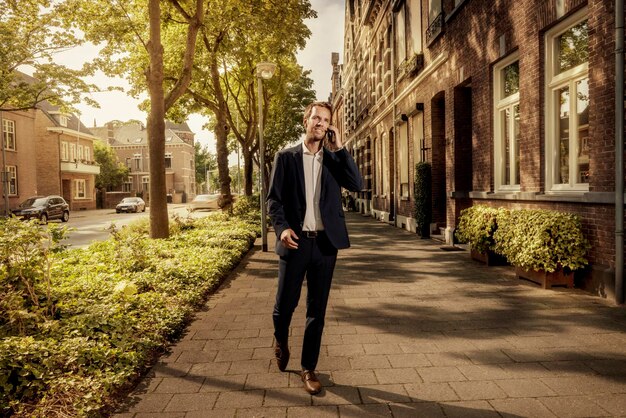 Netherlands, Venlo, businessman on cell phone walking on pavement