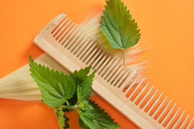イラクサの葉、竹の櫛と髪の束、イラクサのオレンジ色の背景を持つ自然なヘアケア製品
