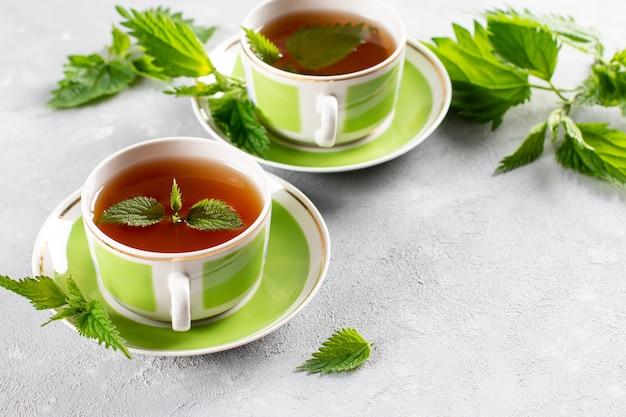 Nettle tea in two cups, fresh stinging nettle herbs