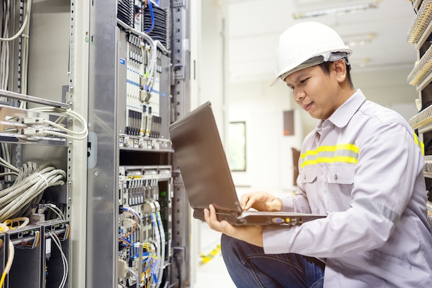 Network administrator holding laptop in hand working Configuration with core switch on rack cabinet in data center