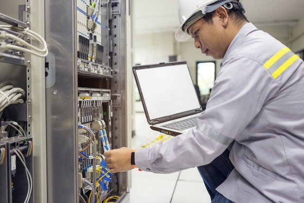 Network administrator holding laptop in hand working\
configuration with core switch on rack cabinet in data center