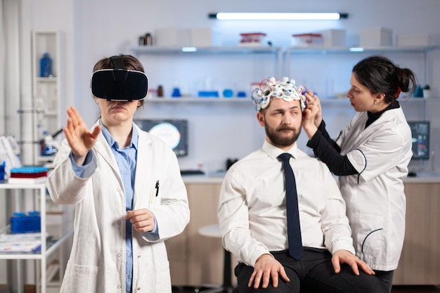 Neurologist doctor gesturing wearing virtual reality headset and assistant adjusting patient sensor that read brain activity , nervous system. Neuroscientist analysing diagnosis.