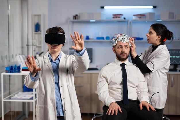 Neurologist doctor wearing virtual reality headset while researcher woman adjusting eeg scanner of man patient analyzing brain activity during neurology experiment. scientist engineer using high tech