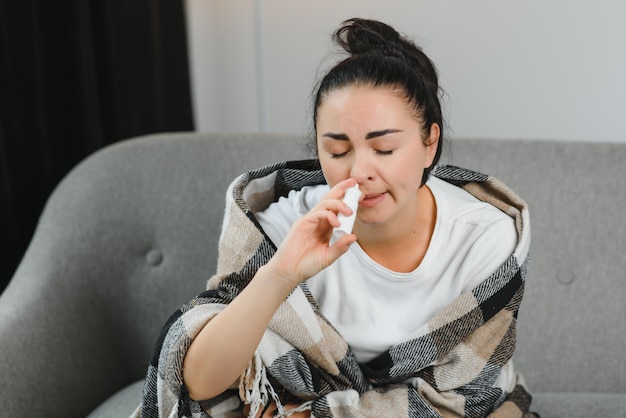 Neusspray in de hand van zieke jonge vrouw die op de bank zit Allergische rhinitis symptomen en behandeling