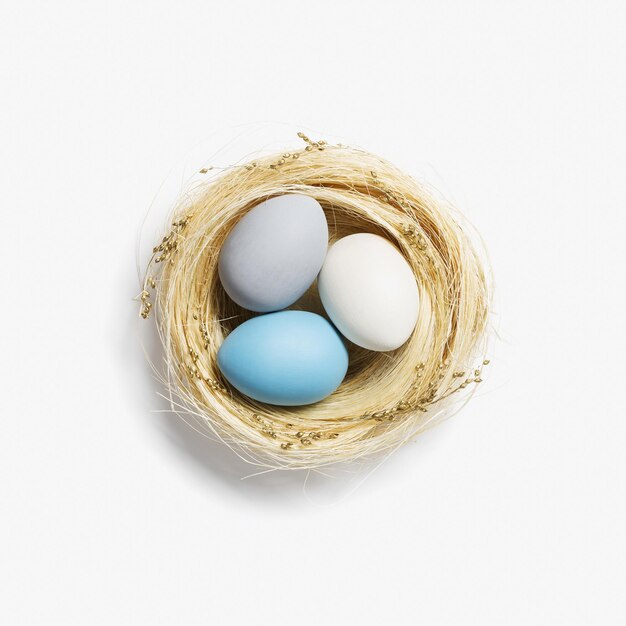 Neutral colored eggs in nest straw on white background Stylish egg for easter spring holiday Top view decorative pastel colored Easter eggs minimal style card