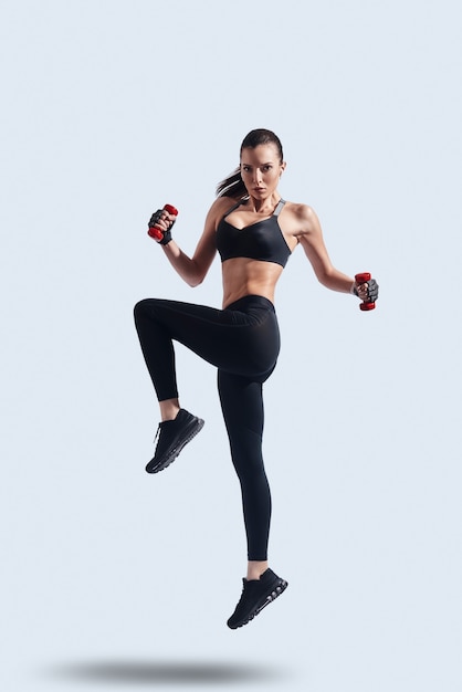 Never give up! Full length of attractive young woman in sports clothing looking at camera while hovering against grey background