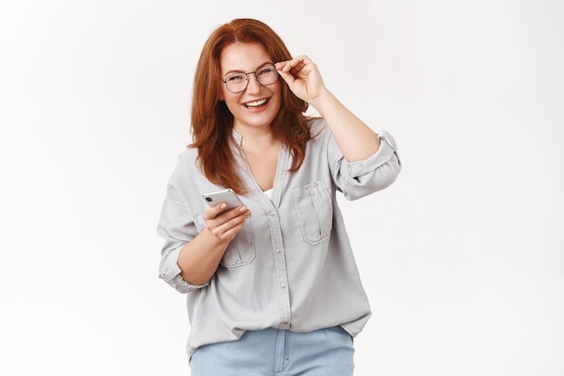 Never was easier Cheerful carefree happy emotive redhead middleaged woman checking glasses hold smartphone laughing pleased joyful camera get used new phone managing schedule via cellphone