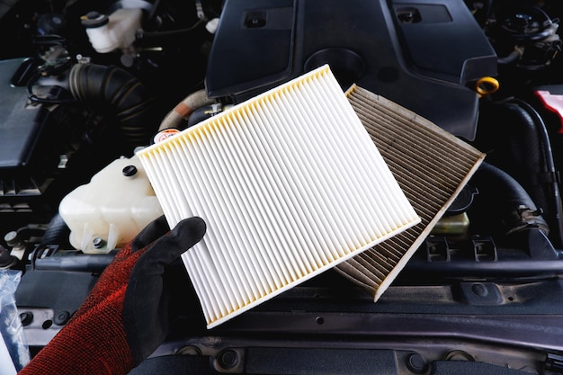 New air filter in a hand and old filthy filter placed on the\
car engine compartment