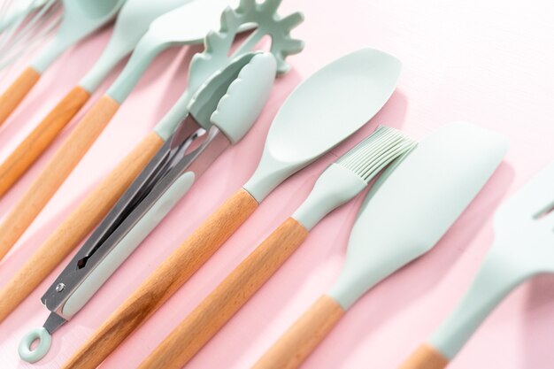 New blue silicone kitchen utensils with wooden handles on a pink background.