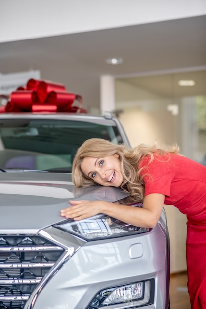 New car. Pretty woman in a red dress looking excited standing near the new car