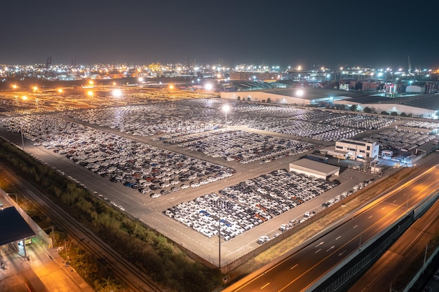 New cars parked at distribution center automobile factory at night with lights aerial view