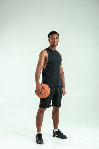 New champion. Full-length of confident young african man in sport clothing carrying a basketball ball and looking at camera while standing against grey background. Basketball. Professional sport