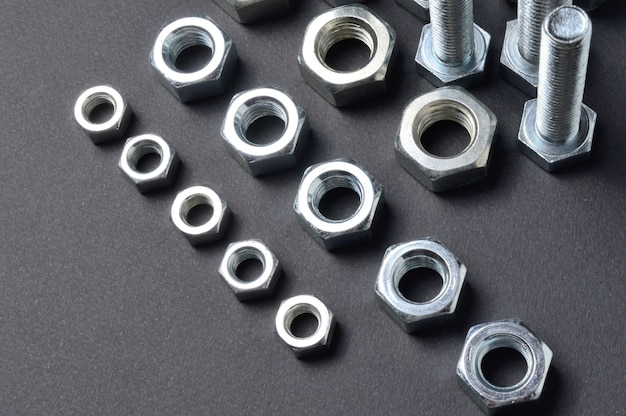 New chrome nuts and bolts of different sizes are laid out against a dark background. close-up.