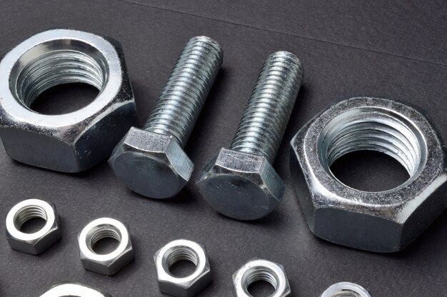 New chrome nuts and bolts of different sizes are laid out against a dark background. close-up.