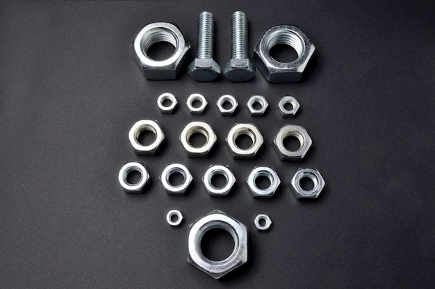 New chrome nuts and bolts of different sizes are laid out against a dark background. close-up.