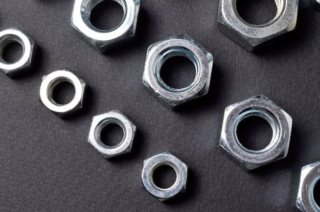 New chrome nuts of different sizes are laid out against a dark background. close-up.