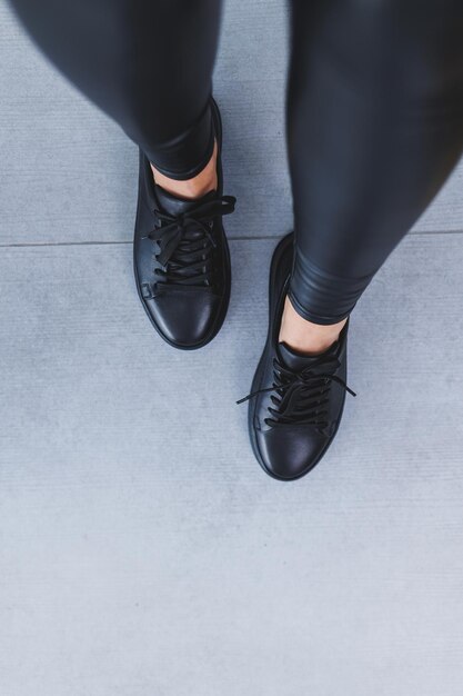 Foto nuova collezione di scarpe da donna in pelle gambe femminili in primo piano in scarpe da ginnastica nere con lacci scarpe per la primavera e l'estate