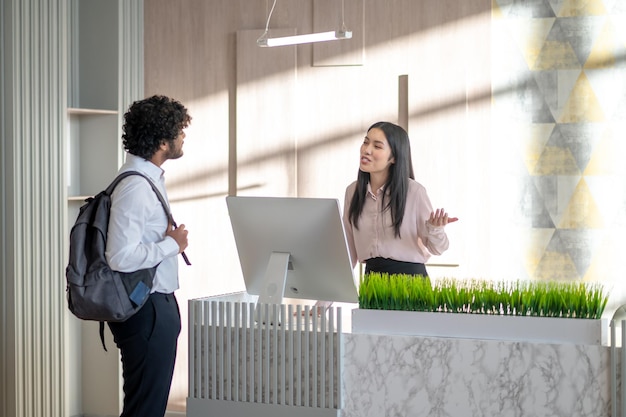 New comer. Indian young man with backpack talking to a girl on reception