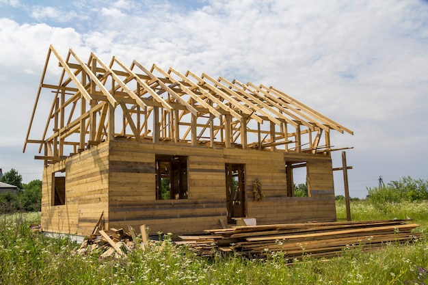 New cottage of natural ecological lumber materials under construction in green field. Wooden walls and steep roof frame. Property, investment, professional building and reconstruction concept.