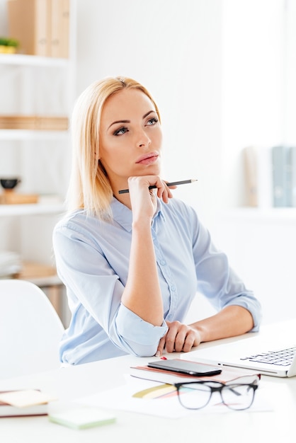 Nuovo giorno nuove decisioni. giovane e bella donna pensierosa che tiene la mano sul mento e sembra pensierosa mentre è seduta al suo posto di lavoro