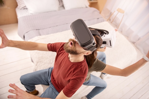 New emotions. Top view of emotional handsome man staring up while sitting on the bad and wearing VR headset