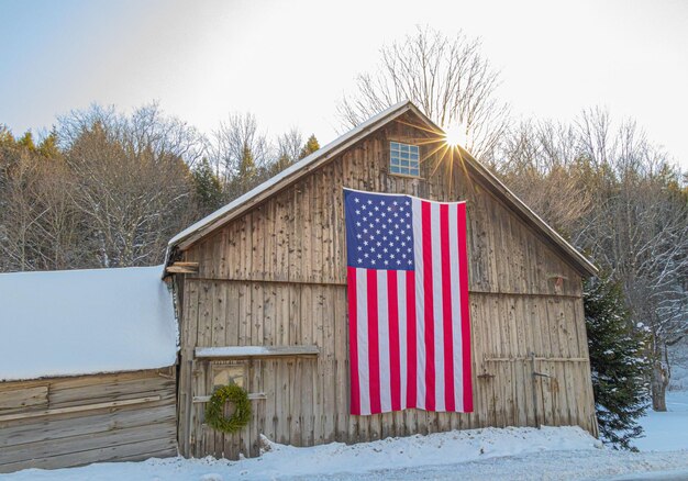 アメリカ国旗を掲げた冬のバーモントの新しいイングランドの納屋