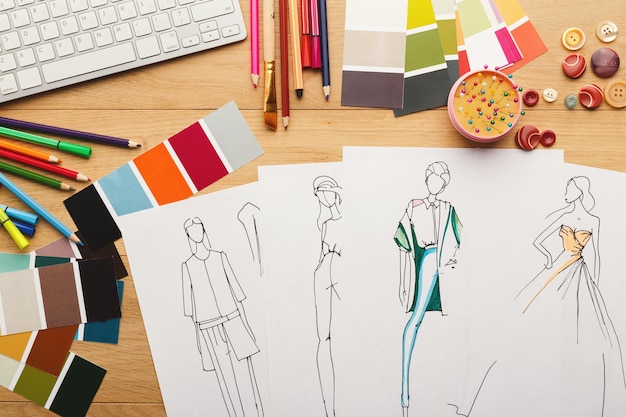 Foto sfondo della nuova collezione di moda. schizzi disegnati a mano di vestiti, campioni di colore e fili sul tavolo di legno, vista dall'alto. creatività, sartoria e concetto di design
