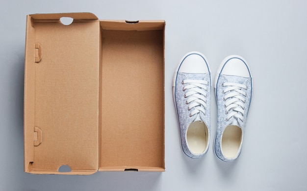 New fashionable sneakers and empty cardboard box on gray surface. 