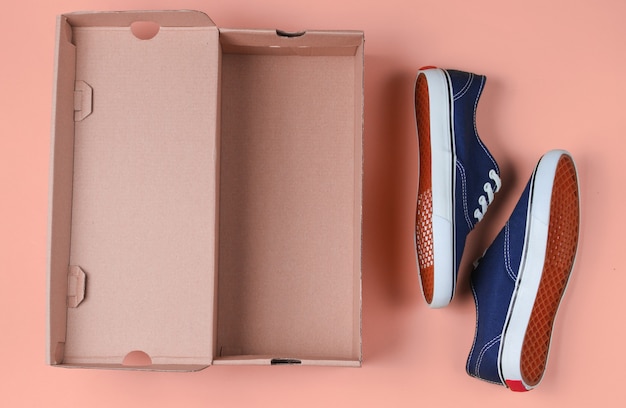 New fashionable sneakers and empty cardboard box on pink