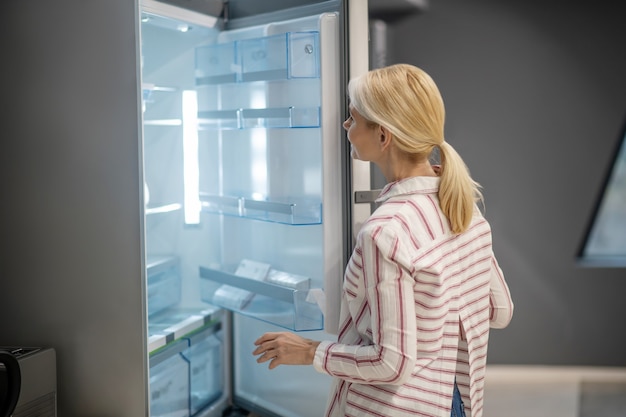 New fridge. Blonde female customer choosing a fridge in a megastore