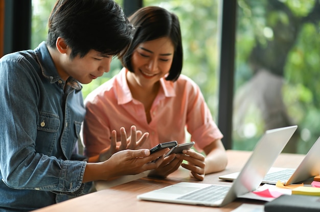 La nuova generazione di giovani uomini e donne sta usando lo smartphone per cercare informazioni e laptop sulla scrivania.