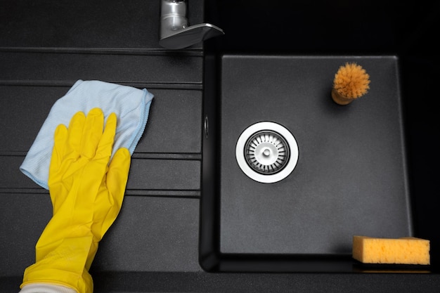 New granite kitchen sink black Cleaning female hand washes the sink with a rag without traces