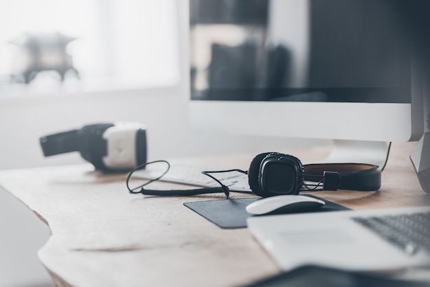 New innovations. Headphones and VR headset laying on the office desk and near laptop and computer