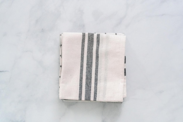 Новые кухонные полотенца с простым черным узором, сложенные на мраморной стойке.