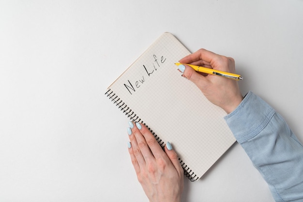 白い背景にノートに書かれた新しい人生の言葉コピーブックを持つ女性の手のトップビュー