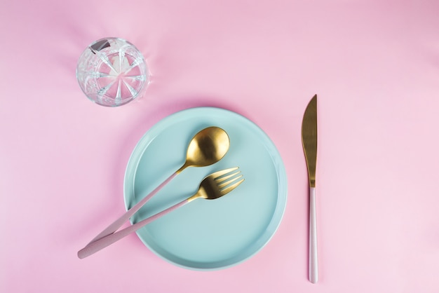 New luxury Golden cutlery with glass, blue plate on pink 