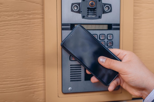 A new and modern smart intercom with a digital camera close-up. Built into the wall. A man's hand holds the phone next to him.