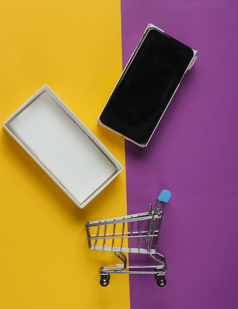 New modern smartphone in box and mini shopping trolley on colored