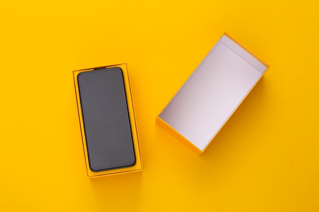 Nuovo smartphone moderno in una scatola di imballaggio su giallo. minimalismo.