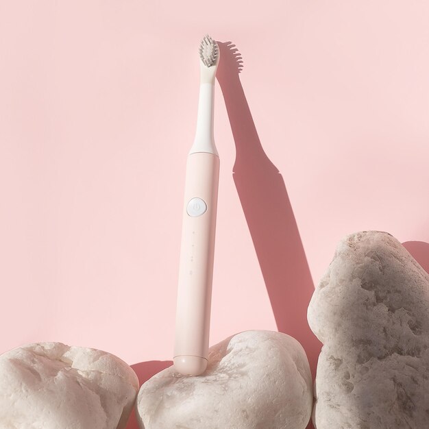 新しい現代の超音波歯ブラシ。ピンクのパステルカラーの背景に白い石で歯科医療用品。口腔衛生、歯と歯茎の健康、健康な歯。歯科用製品超音波振動歯ブラシ。