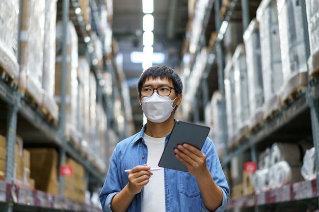 New Normal Asian men, staff, product wearing face mask. counting Warehouse Control Manager Standing, counting and inspecting products in the warehouse