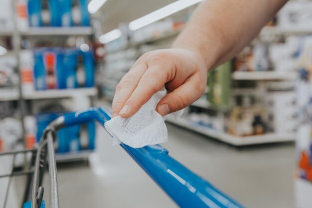 A new normal closeup of man hand cleaning shopping cart handle with disinfecting wet wipe