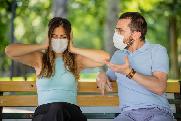 New normal concept after the pandemic an arguing couple view man is dictating woman close ears and unconcerned they are wearing a mask