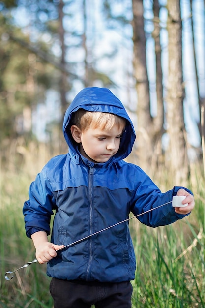 Nuova normale fase di fuga, passeggiate nella natura selvaggia e attività ricreative all'aperto in famiglia. bambini che cucinano e degustano marshmallow fritti sul fuoco, escursione nel fine settimana, stile di vita