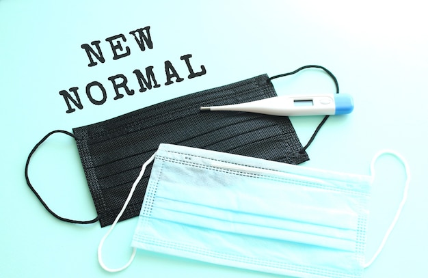 파란색 배경에 파란색과 검정색 의료 마스크가 옆에 놓여 있는 NEW NORMAL 글자. 의료 개념입니다.