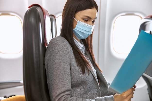 New order in airplane. Woman is sitting in mask before fly