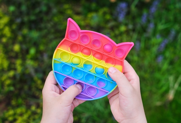 Photo new popular silicone popit toy, baby is playing with it. rainbow trendy pop it fidget toy.