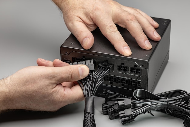 A new power supply for a desktop computer with a set of wires and cables. Connection, men's hands.